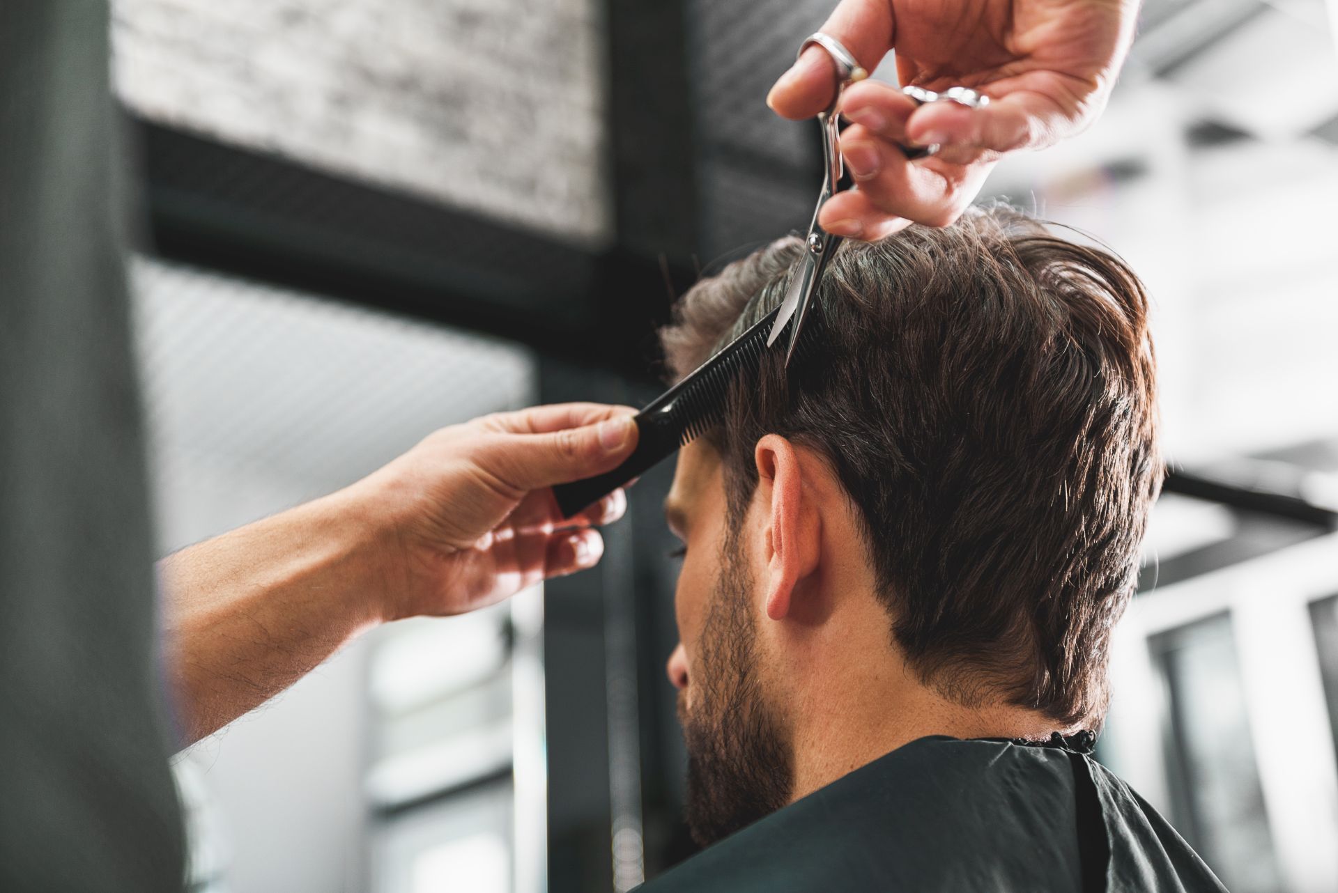 Skillful coiffeur doing haircut for young man. He is holding scissors and comb